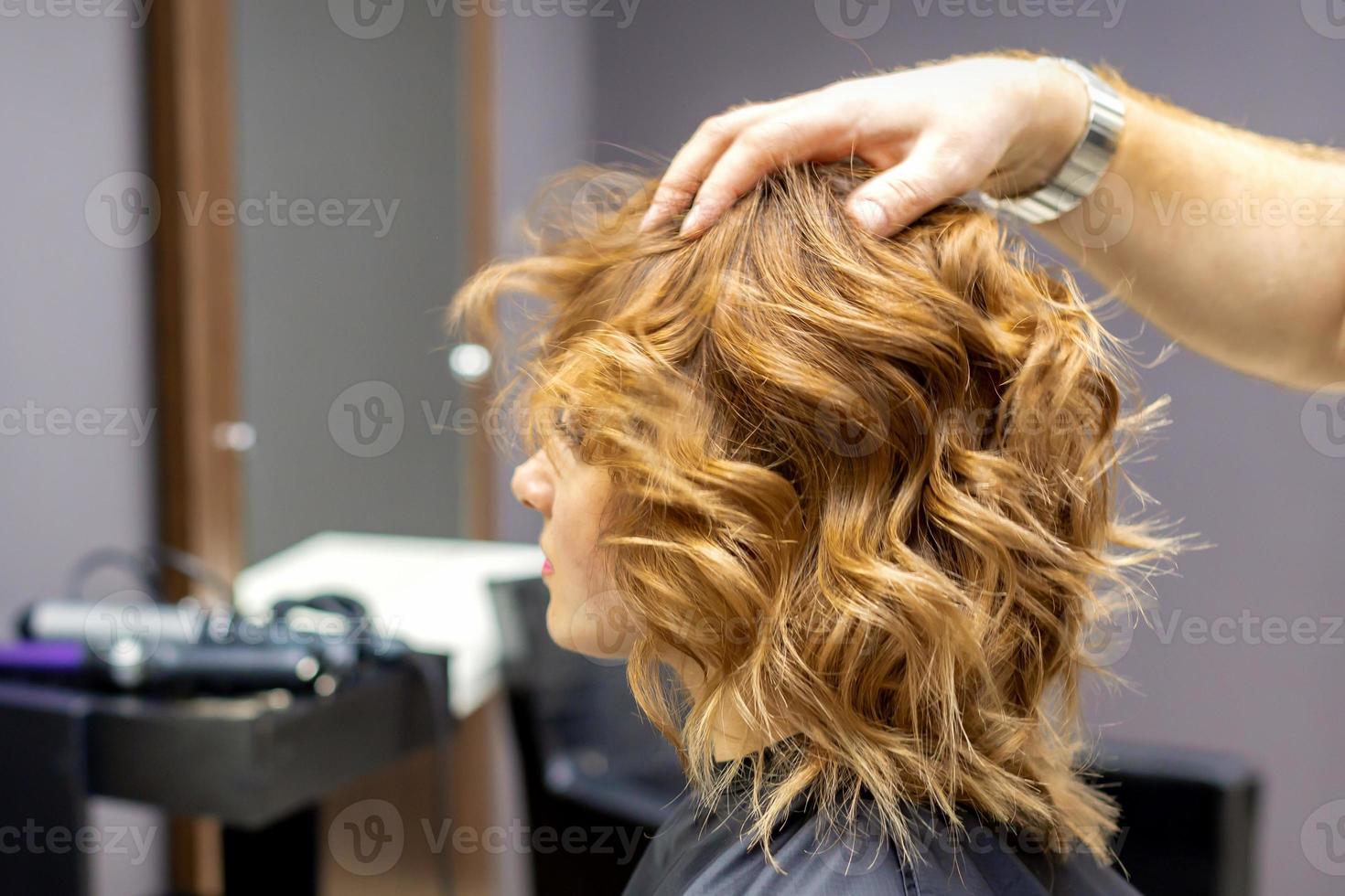 Hairdresser checks curly hairstyle of woman photo