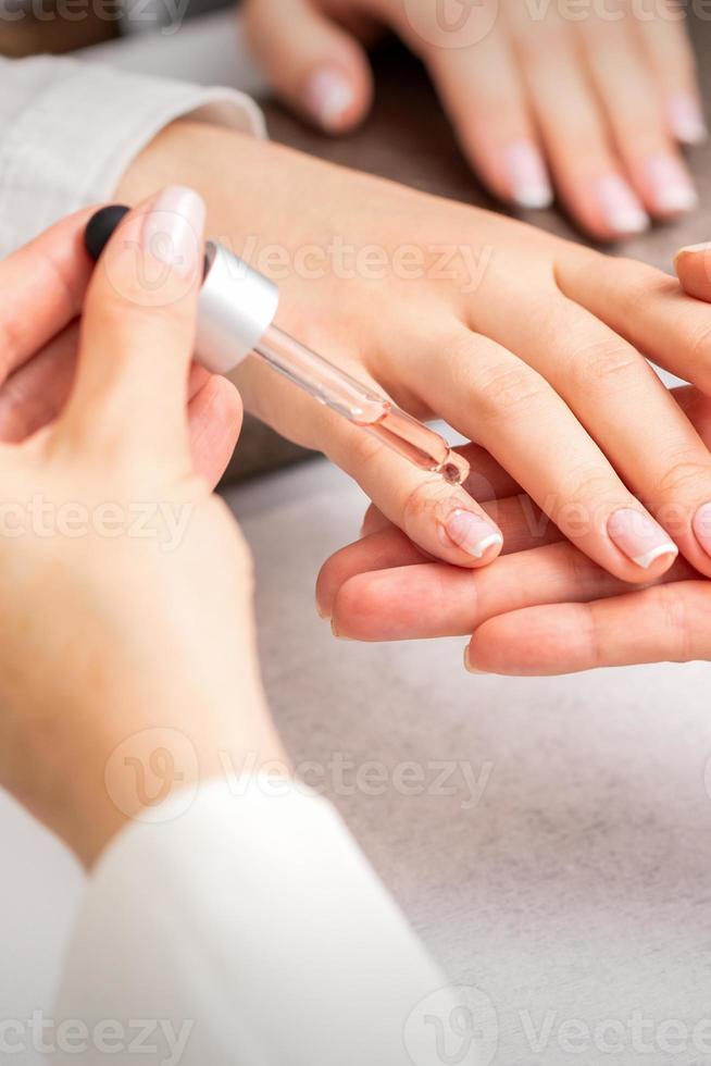 Hand of manicurist pours oil to cuticle photo