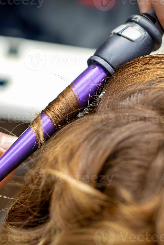 Hairdresser makes hairstyle by curling iron photo