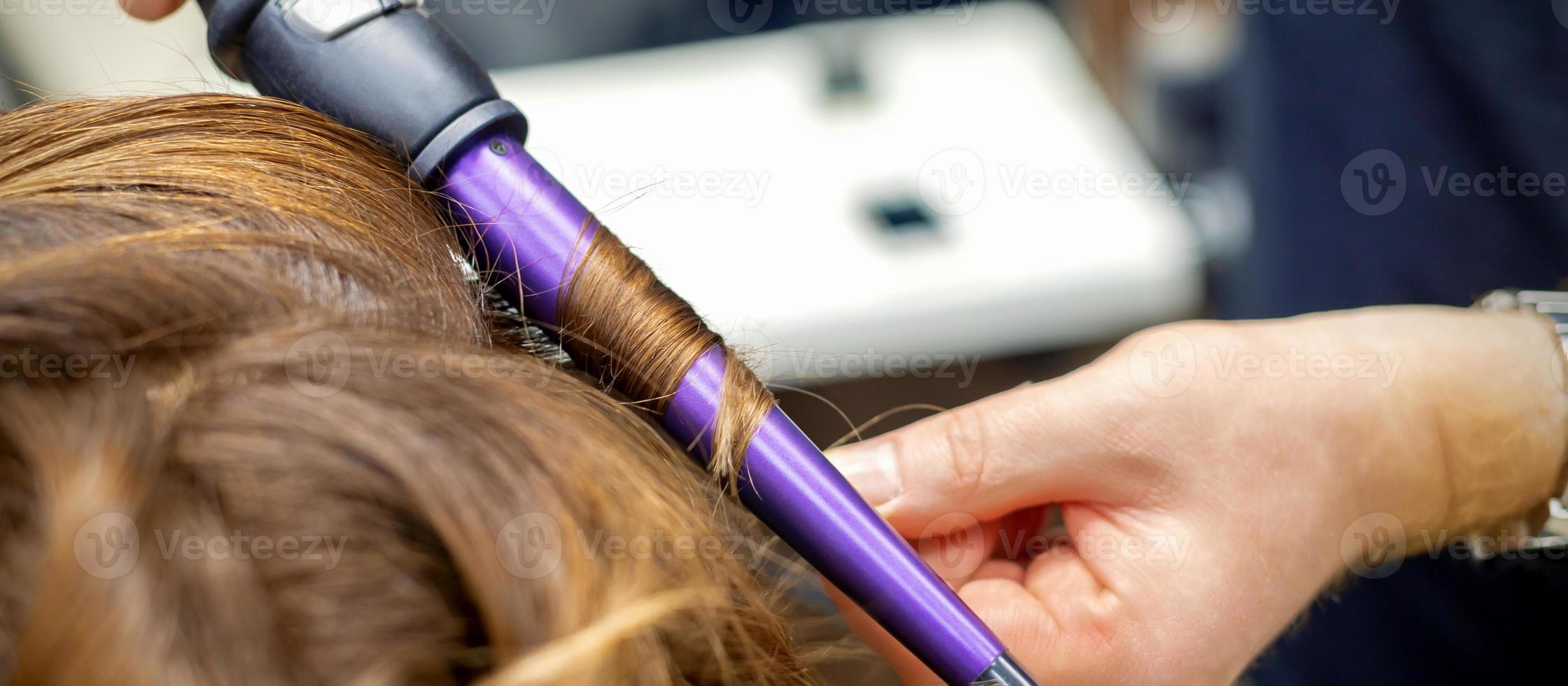 Hairdresser makes hairstyle by curling iron photo