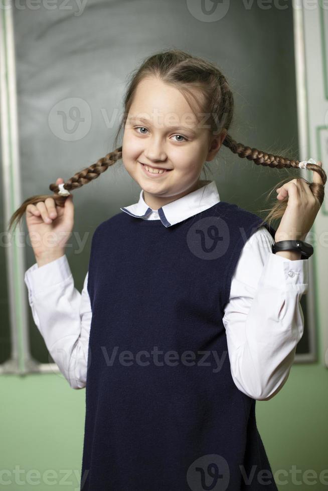 Funny schoolgirl with pigtails, middle school age on the background of the blackboard. photo