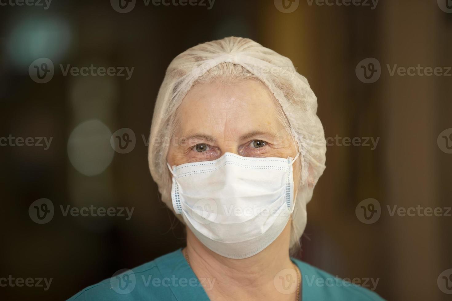 The face of an elderly female doctor or nurse in a medical mask, with kind eyes, close-up. photo