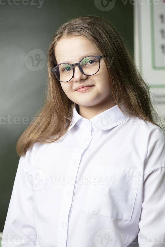 Beautiful girl in glasses of middle school age on the background of the blackboard. photo