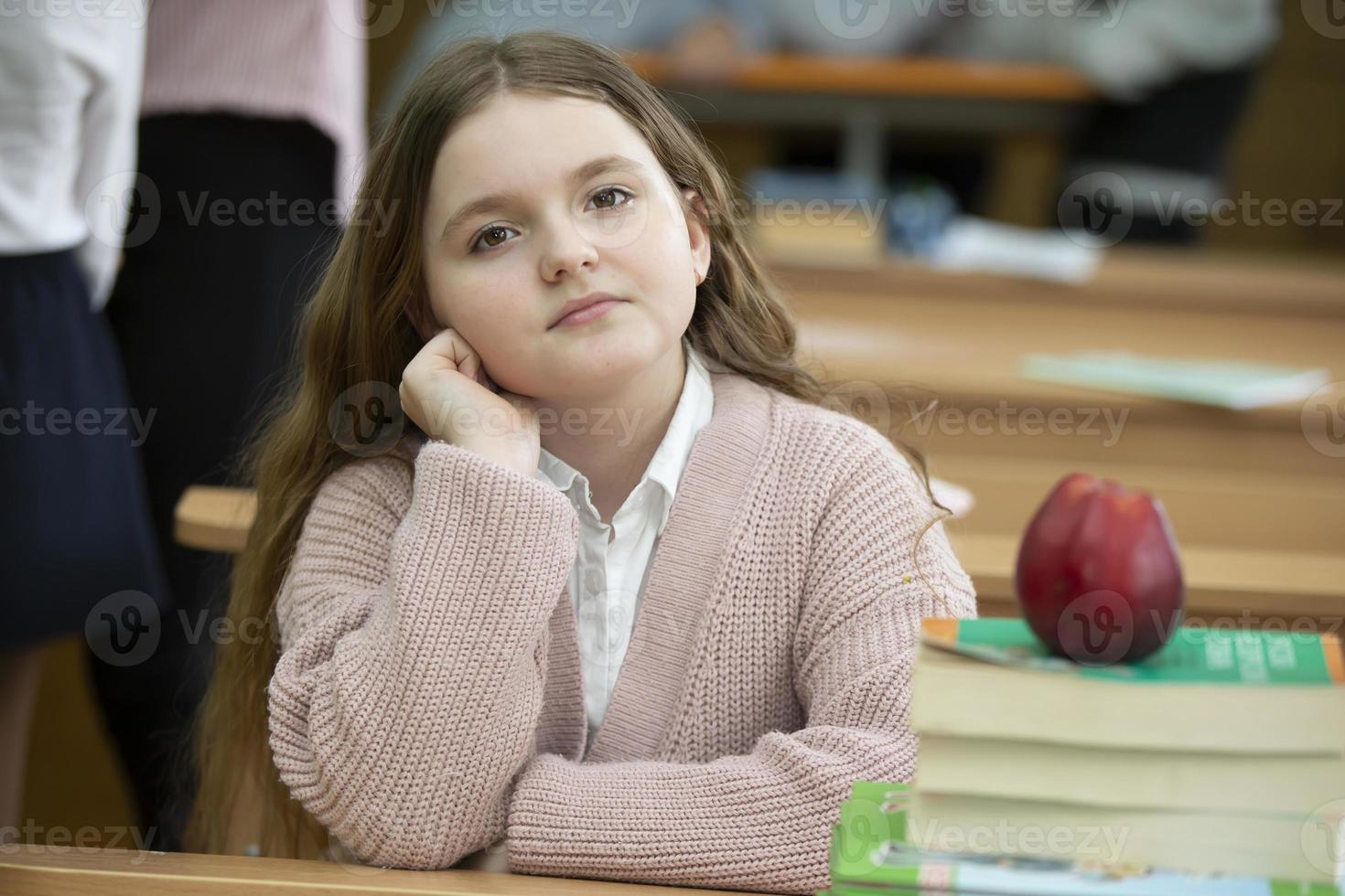 Girl schoolgirl at the desk. Girl in the classroom with books and an apple. Secondary school. Back to school. photo
