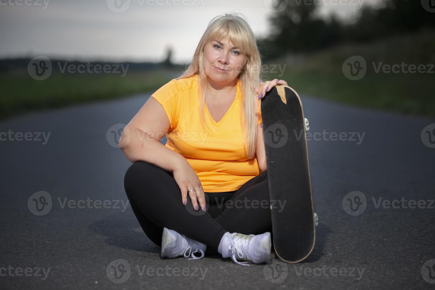 Mujer europea de mediana edad con sobrepeso, en chándal con patineta, practica deportes. foto