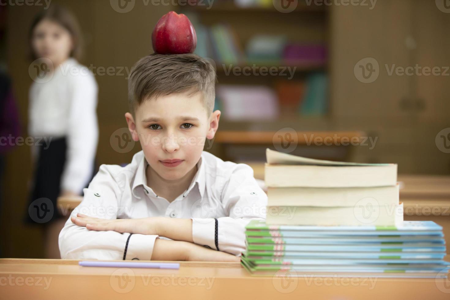 Funny schoolboy at the desk. The boy in the class is playing around, put an apple on his head. Secondary school. Teaching extraordinary children. photo