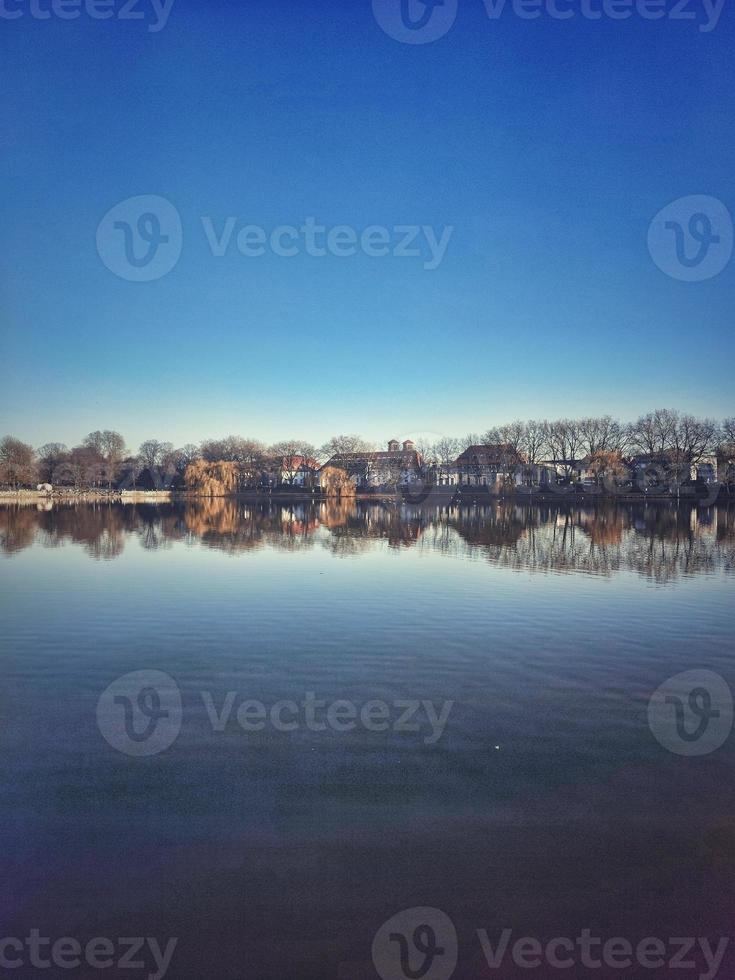 View of lake and houses on the shore in the early morning with blue sky photo