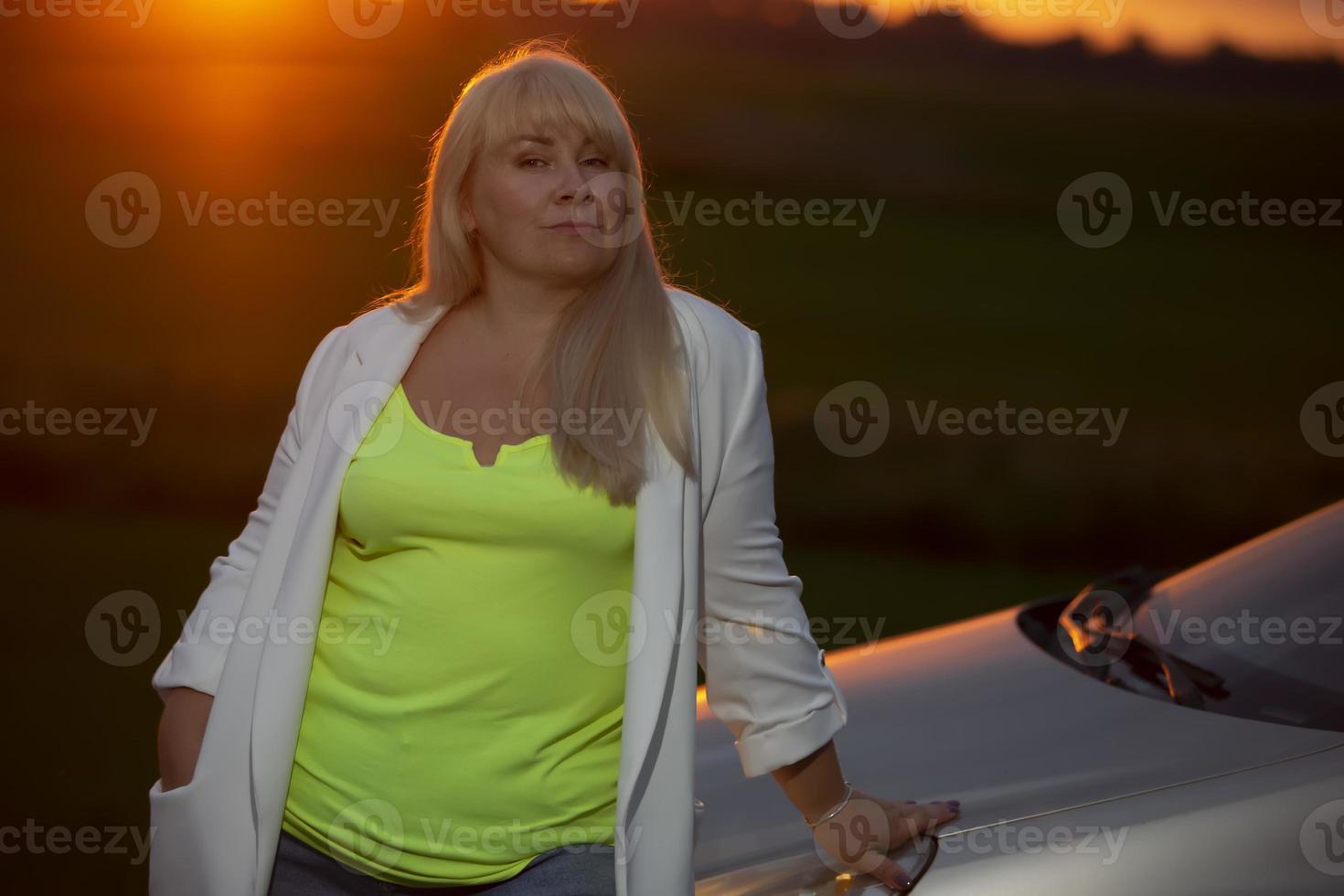 Beautiful middle age blond woman against sunset sky. photo