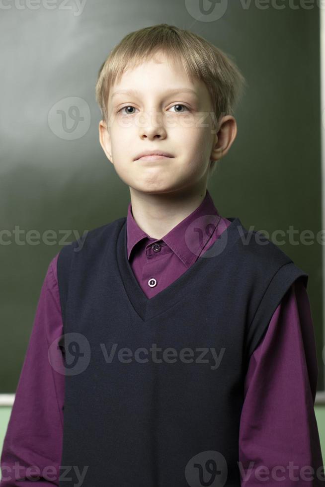 Portrait of a schoolboy at the blackboard. The boy in the classroom is looking at the camera. photo