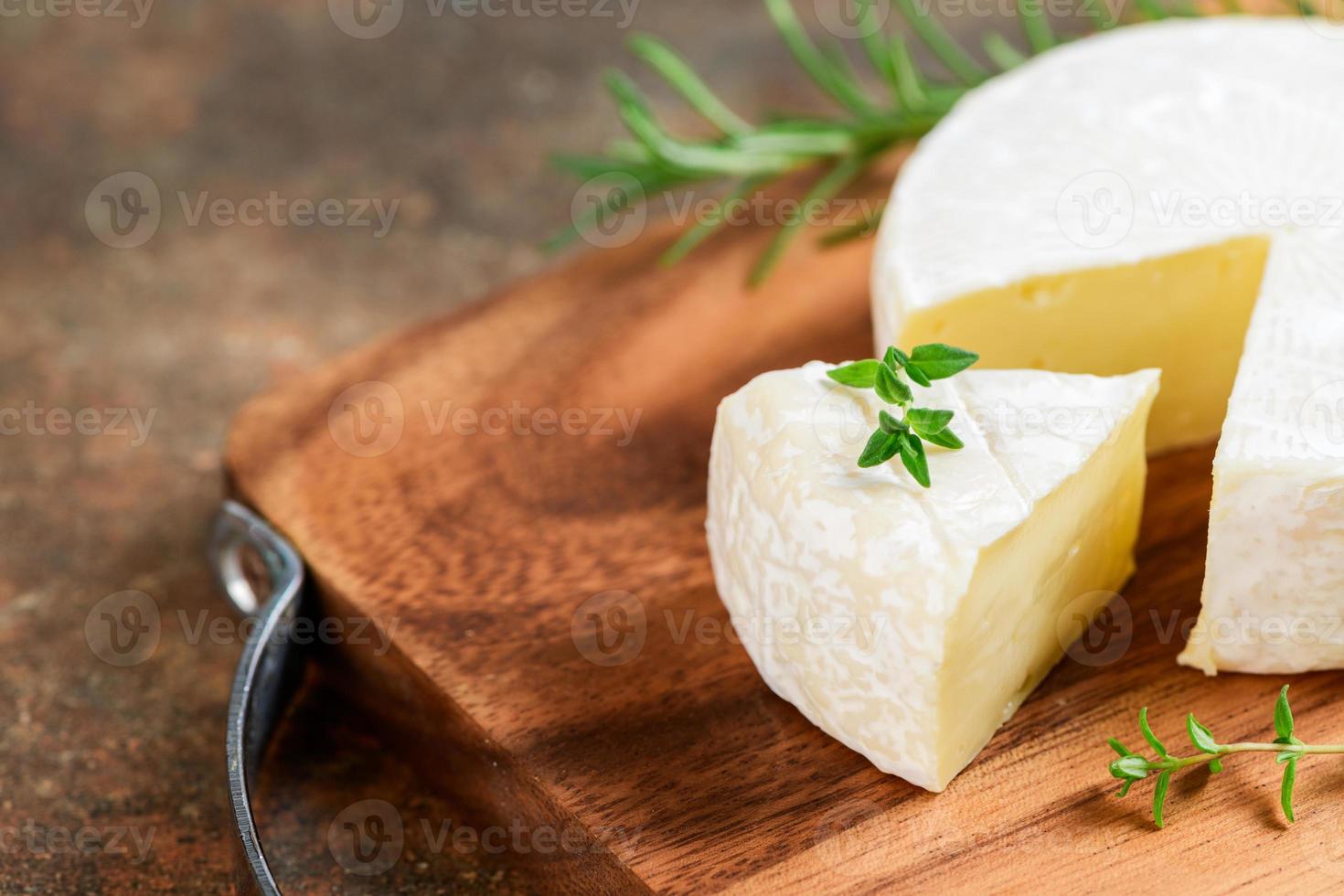 Sliced Camembert Cheese with thyme on wood plate. Camembert is a moist, soft, creamy, photo