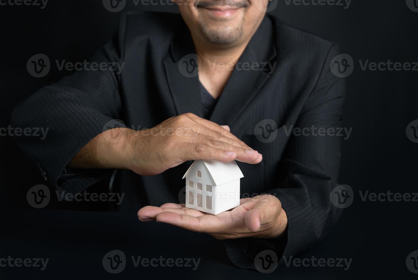 Businessman real estate realtor or house insurance agent making a protecting hands gesture over the house. Property insurance and security concept. photo