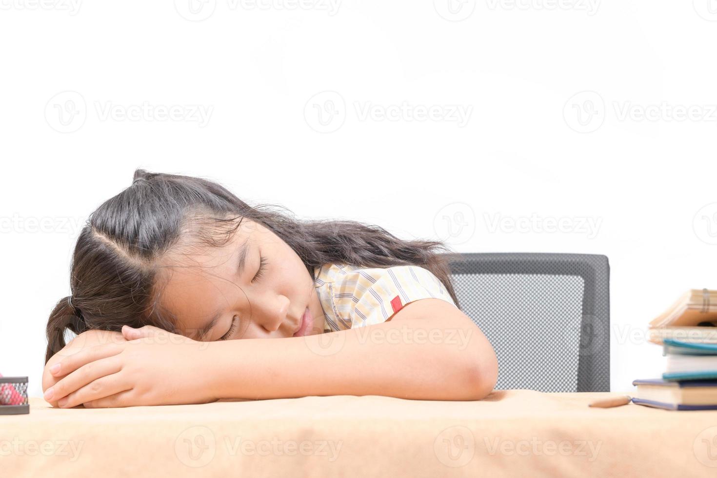 Asian tired little girl sleeping at work desk, lying on table isolated on white, photo