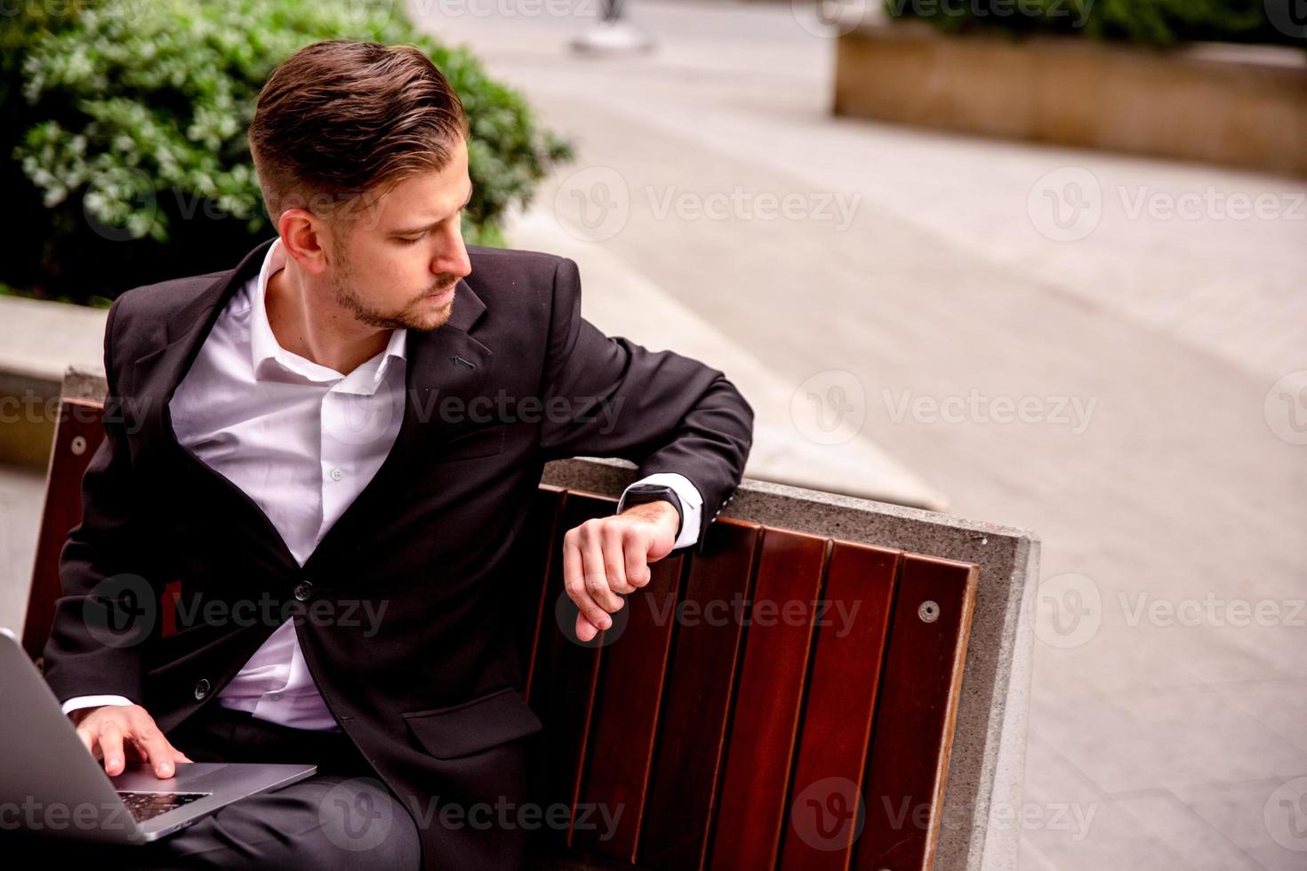 Young guy in a suit works on a computer in the park of a business center photo