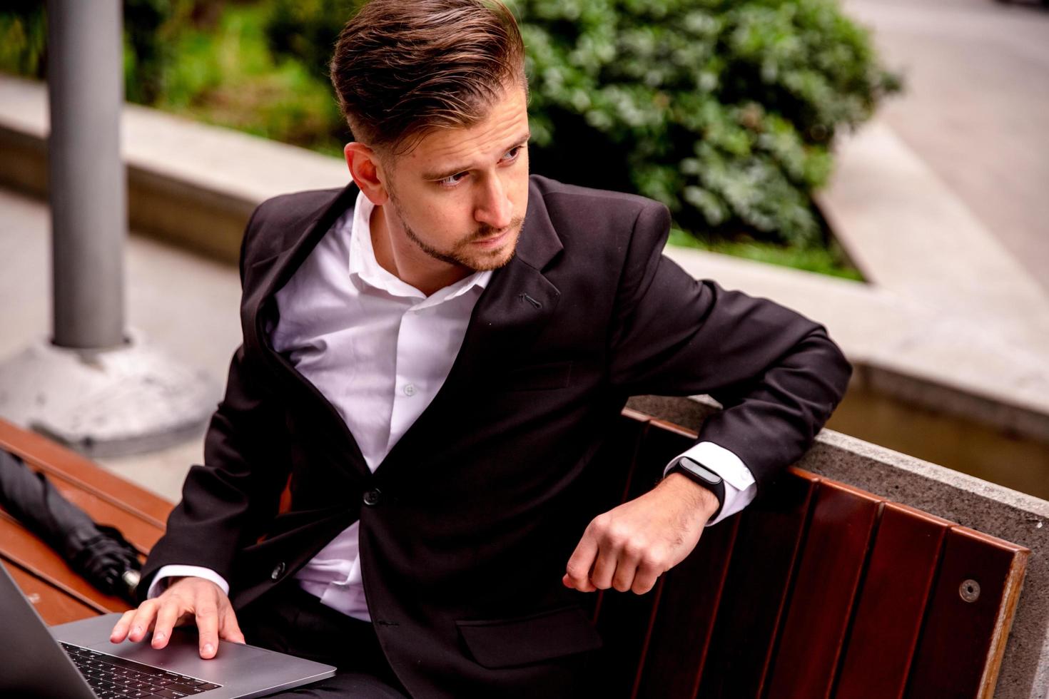 Young guy in a suit works on a computer in the park of a business center photo