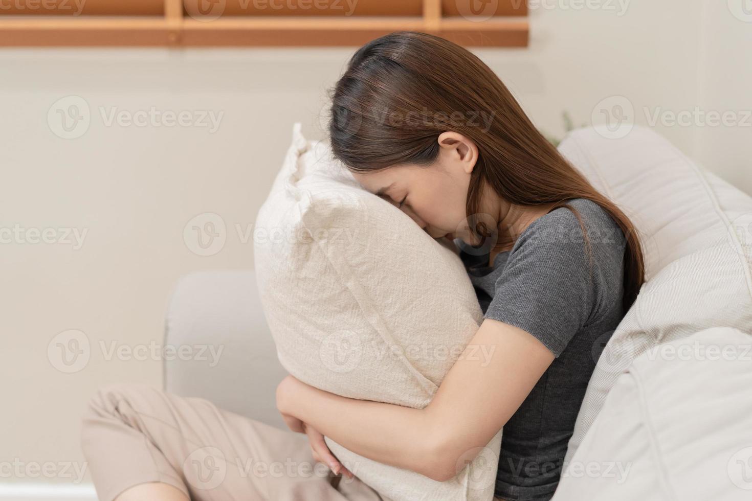 Mental health, depressed sad asian young woman, girl sitting on sofa or couch, cover face with pillow. Difficulty, failure and exhausted. Thoughtful worried suffering depression feeling alone at home. photo