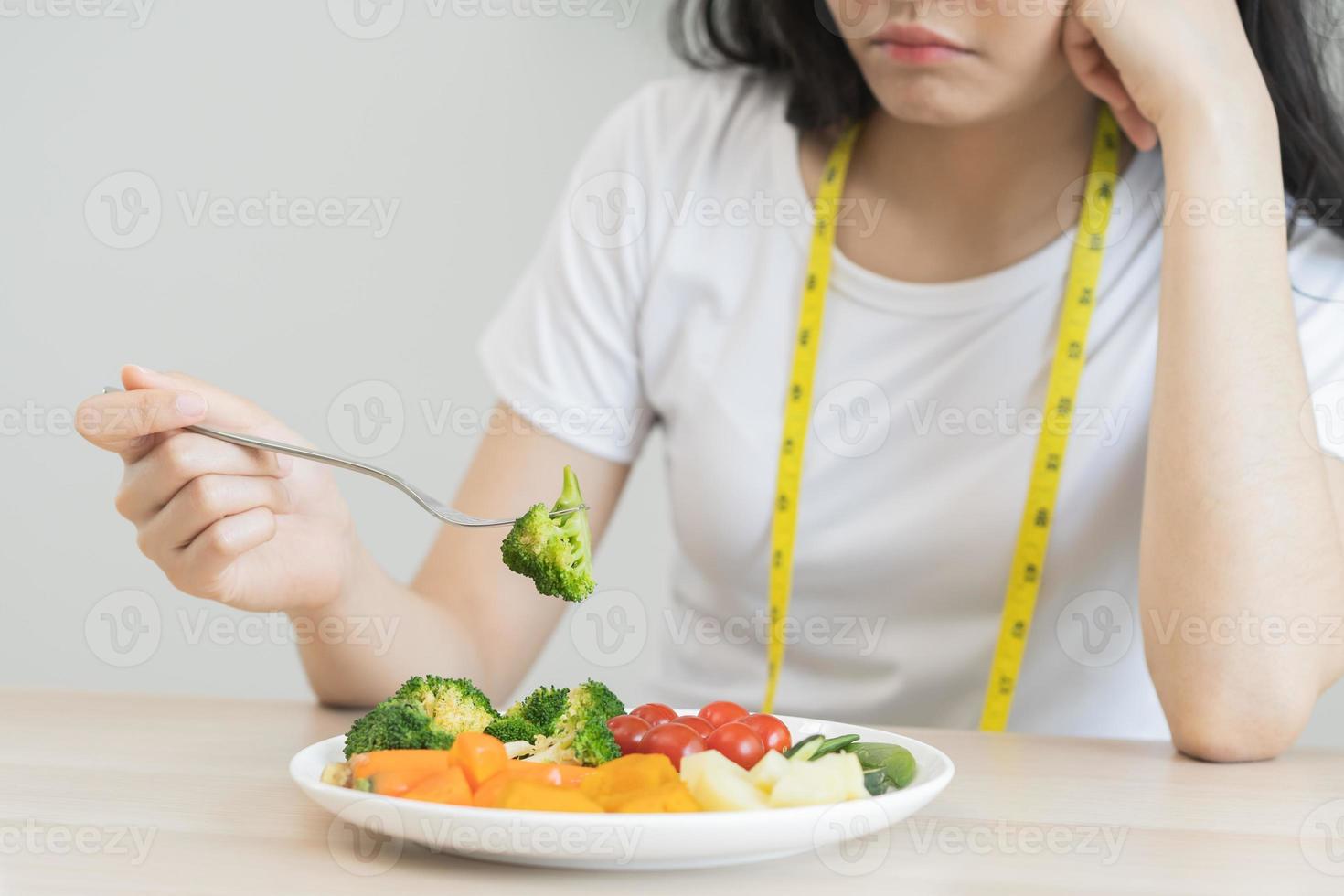 dieta en aburrido. de cerca brócoli infeliz hermosa asiático joven mujer, niña en haciendo dieta, mano participación tenedor en ensalada lámina, disgusto o cansado con comer Fresco vegetales. nutrición de sano comida bueno gusto foto