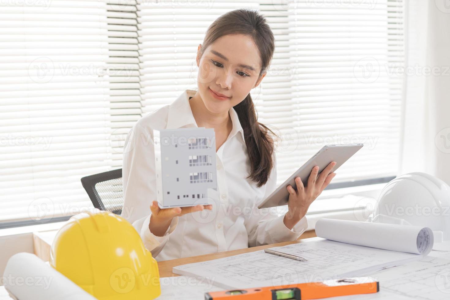 Construction of Engineer, smile architect businesswoman, woman making engineering tools on 3D model house building in office, using tablet for plan with team working on blueprint, design project. photo