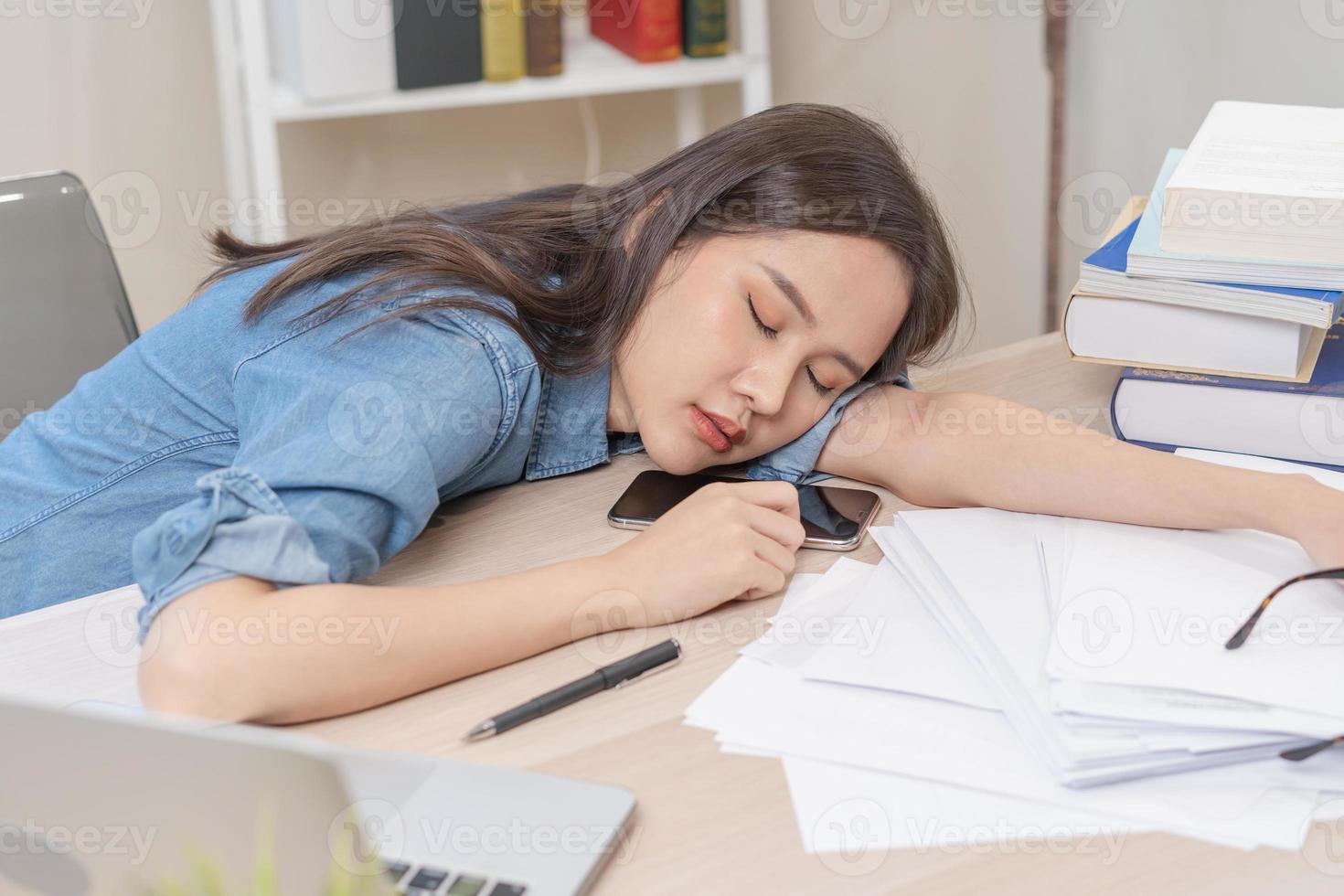 Exhausted, stressed asian young business woman working, took off eye strain glasses, rest nap, sleep on desk after work hard while use laptop computer, office syndrome. Overtime job, tired people. photo