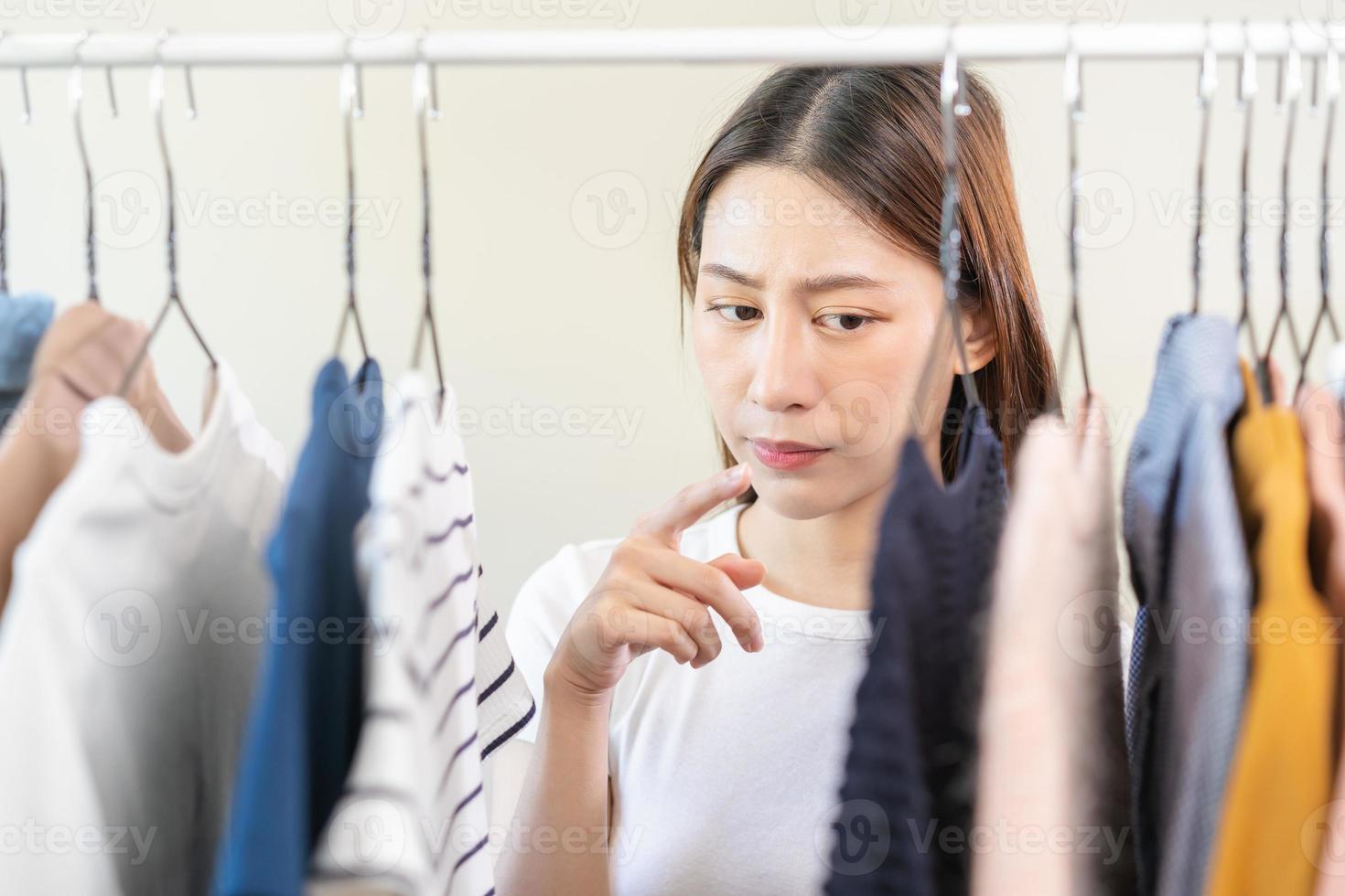 Choice of clothes,Nothing to wear. Attractive asian young woman, girl try on appare, happy choosing dress, outfit on hanger in wardrobe in room closet at home. Deciding blouse what to put on which one photo