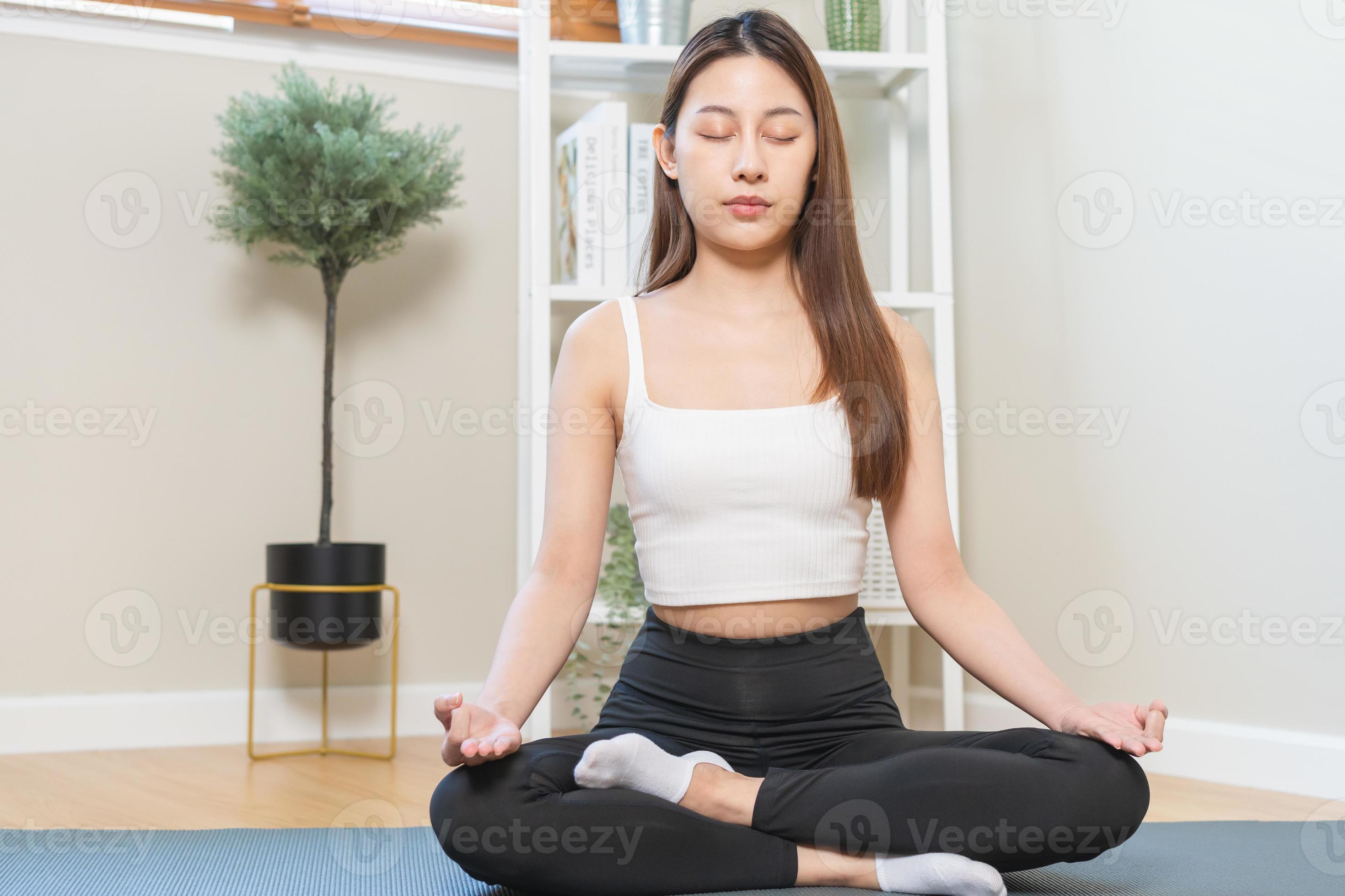 Smiling young girl practicing yoga sitting in lotus pose, meditating in cozy  home interior. Female training for wellness Stock Photo - Alamy