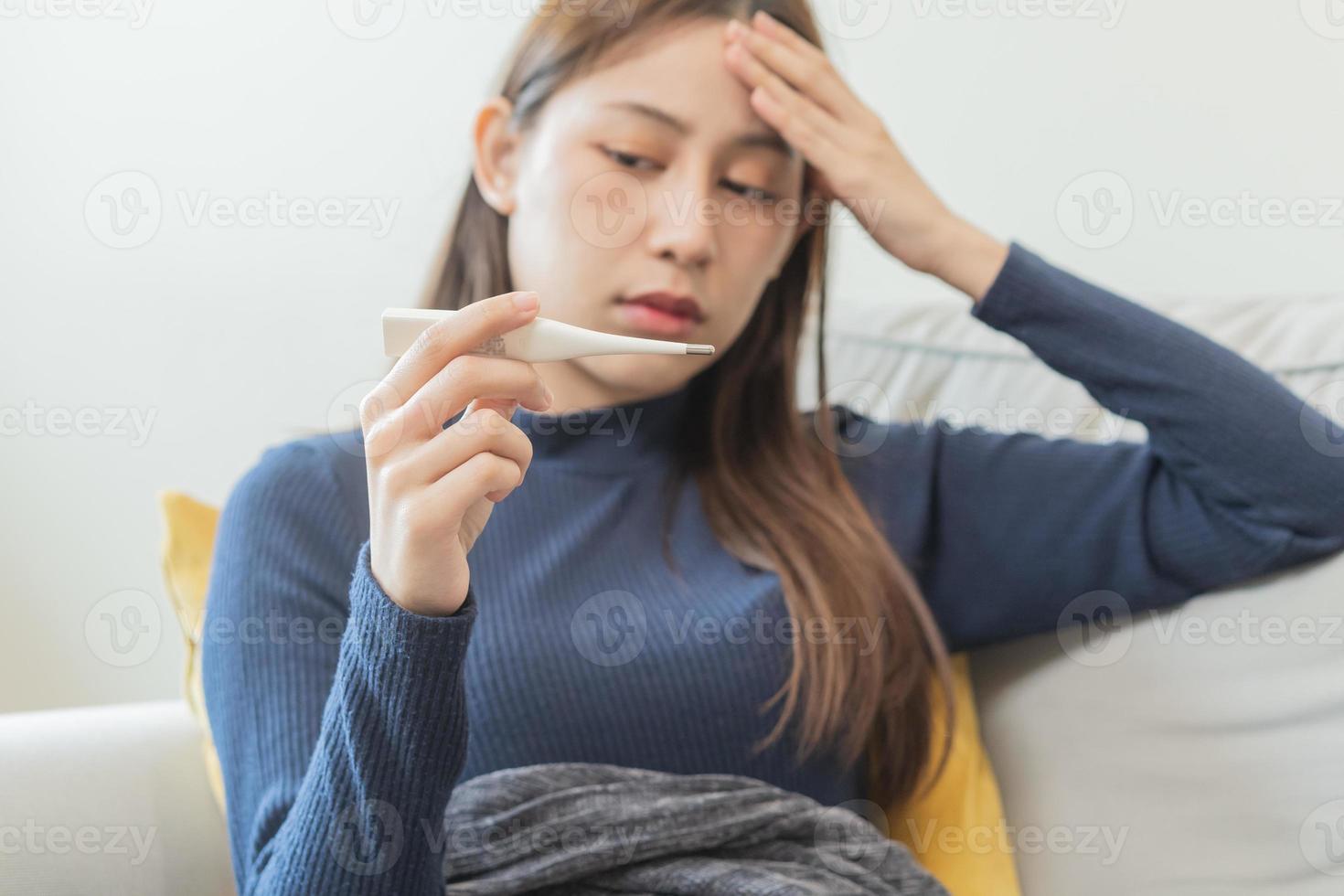 Sick, influenza asian young woman, girl hand in check headache, have a fever, flu and check thermometer measure body temperature, feel illness sitting on sofa bed at home. Health care person on virus. photo