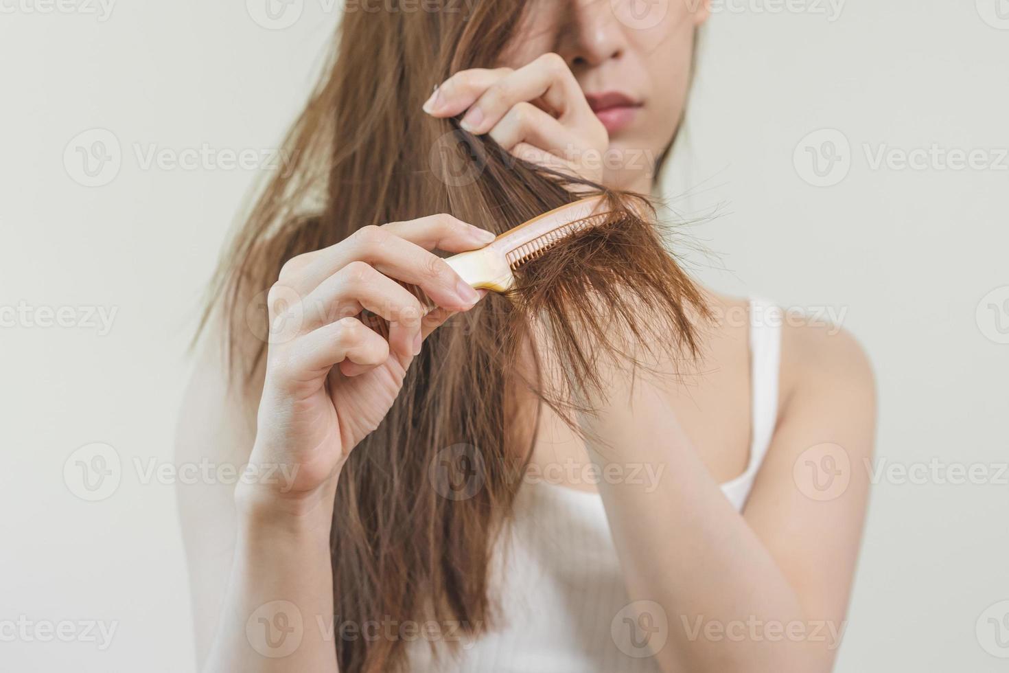 Damaged Hair, frustrated asian young woman, girl hand in holding brush splitting ends messy while combing hair, unbrushed dry long hair. Health care beauty, portrait isolated on white background. photo