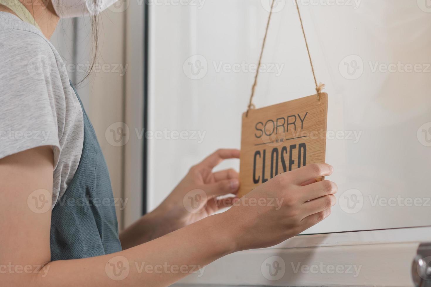 Asian young owner retail,coffee shop woman turning sign board to closed with wearing face mask,protection to pandemic of coronavirus.Close store,restaurant or pub due to lockdown, quarantine of covid. photo