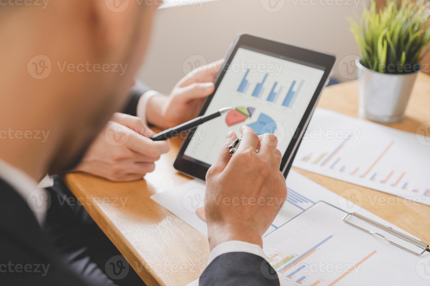 Business meeting, two caucasian, asian group man use tablet brainstorm analyzing on graph data of cost plan or document, paperwork and discussing in board room on table. People working conference room photo