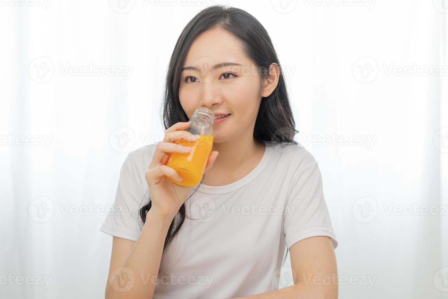 Happy smile asian young woman, girl drinking fresh orange juice in a glass bottle, holding transparent glass in hand, thirsty at home. Healthcare, healthy diet concept, isolated on white background. photo