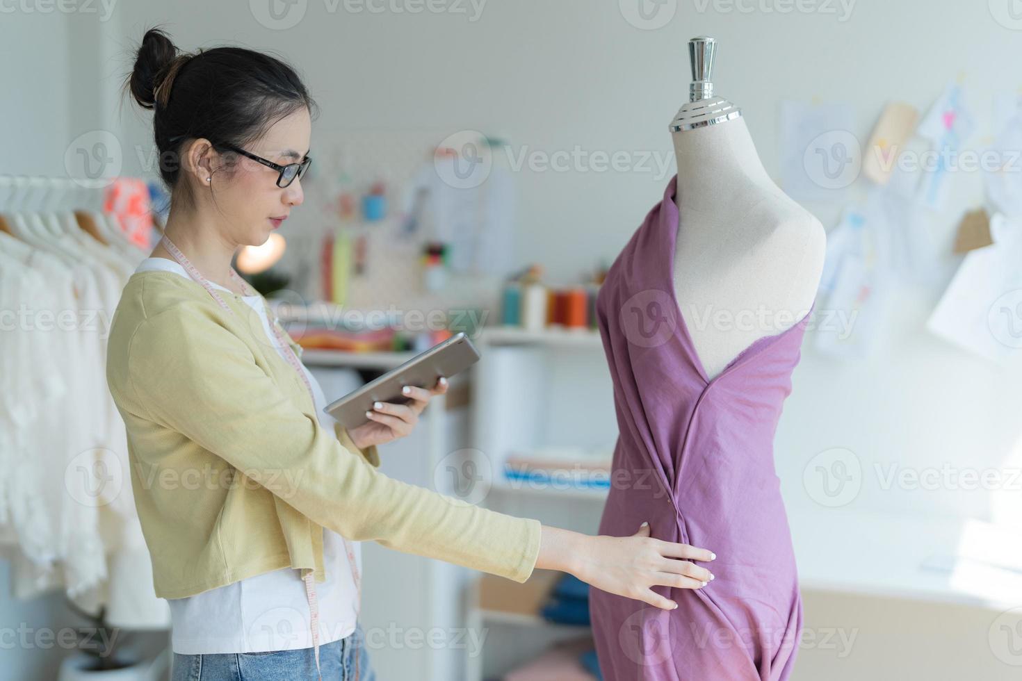 Attractive young fashion designer standing in studio holding tablet next to mannequin. photo