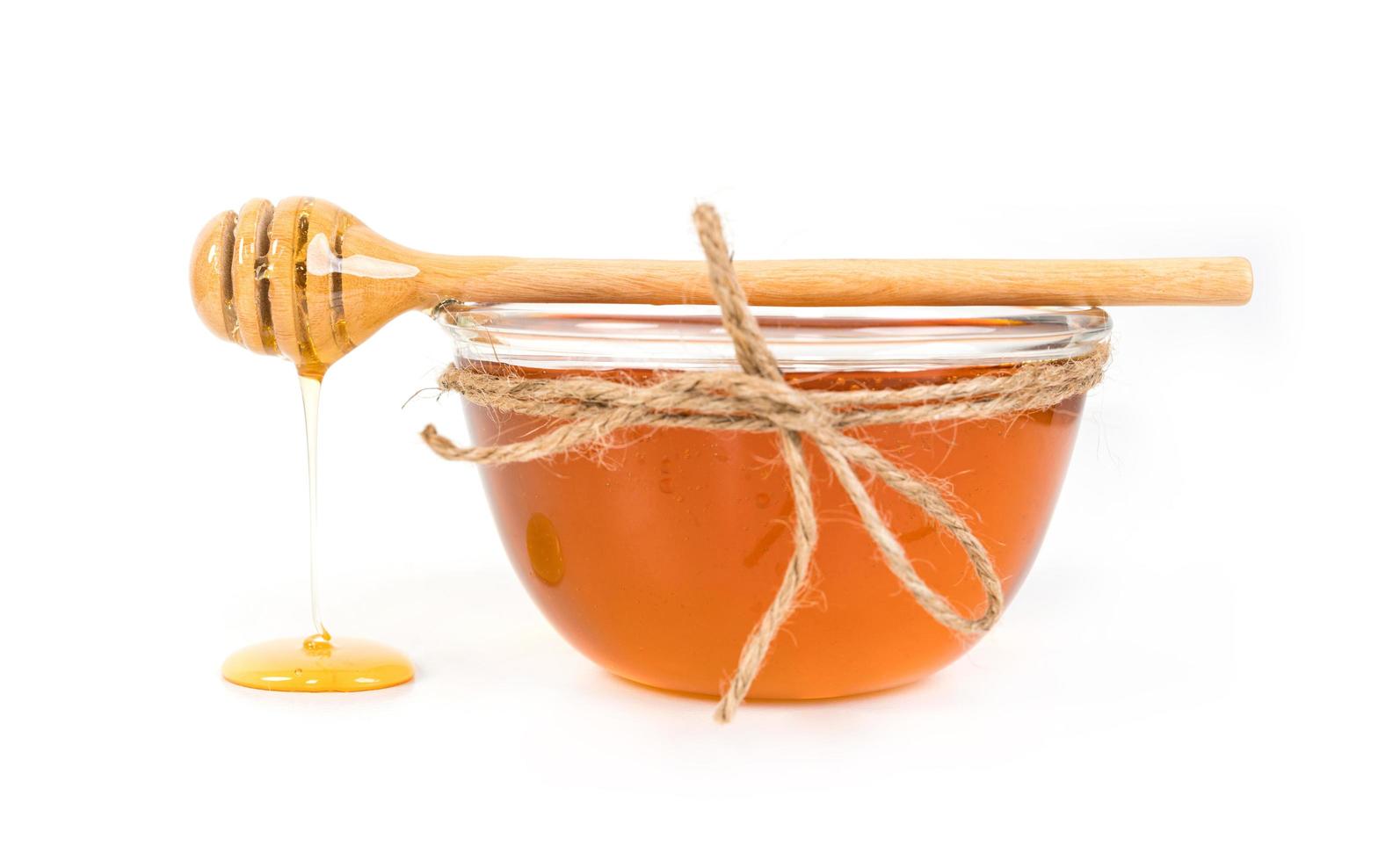 Glass of honey and dipper on white background photo