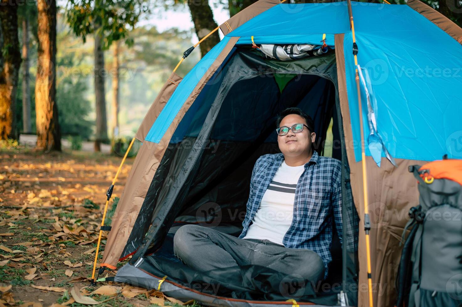 Portrait of Relaxing Asian traveler man glasses looking view while sitting in tent camping photo