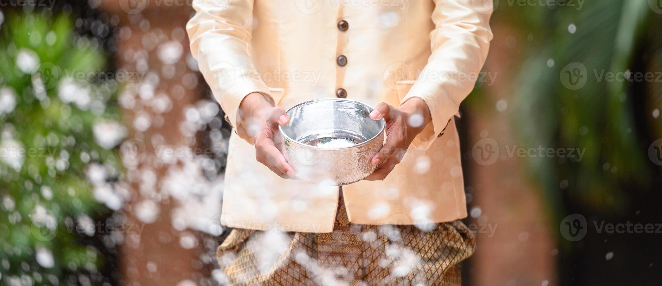 Young man splashing water from bowl on Songkran festival photo
