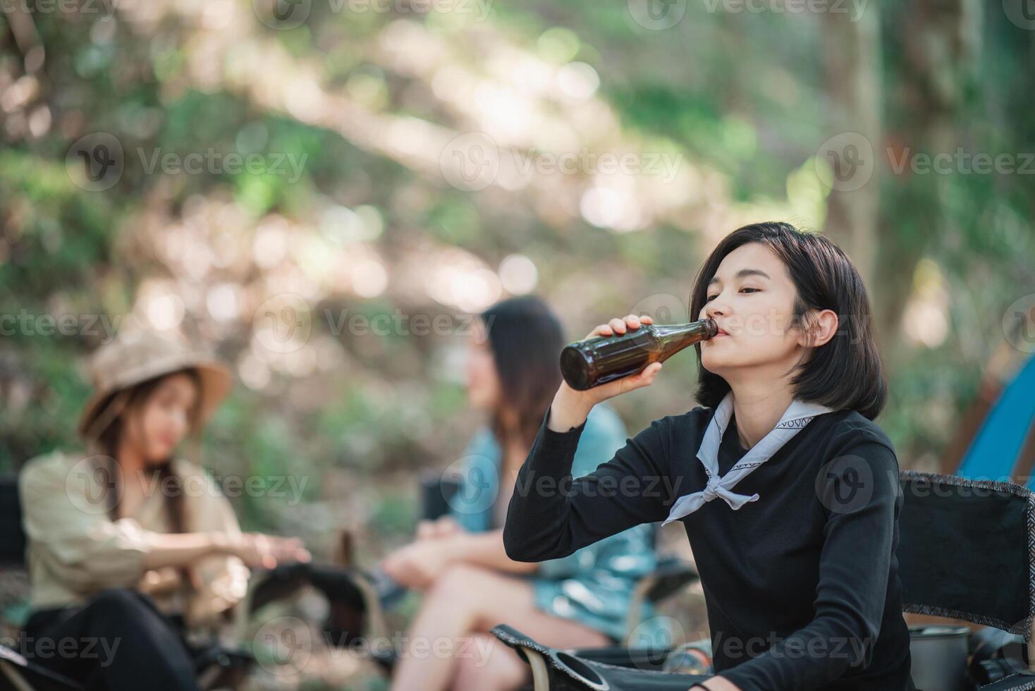 Young women cheer and drink beverage  front of camping tent photo