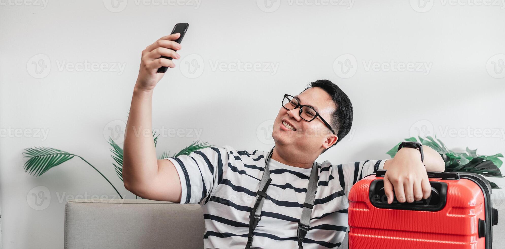 Happy Asian traveler man glasses selfie on smartphone with luggage photo