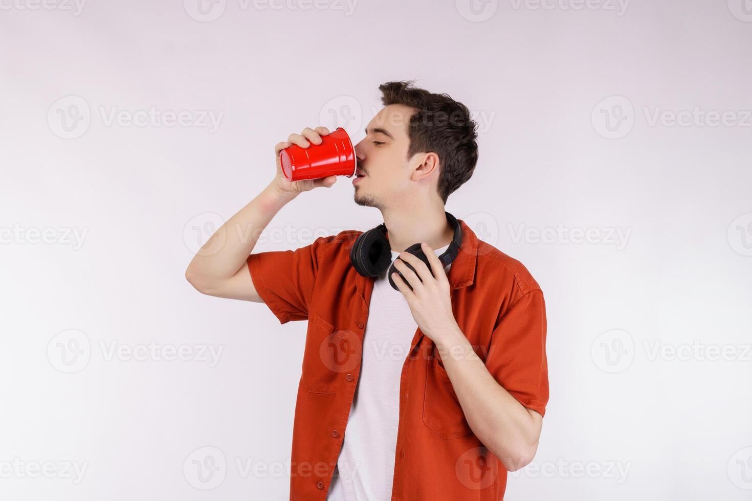 Portrait of a handsome young man with headphone standing and drinking coffee isolated white background photo