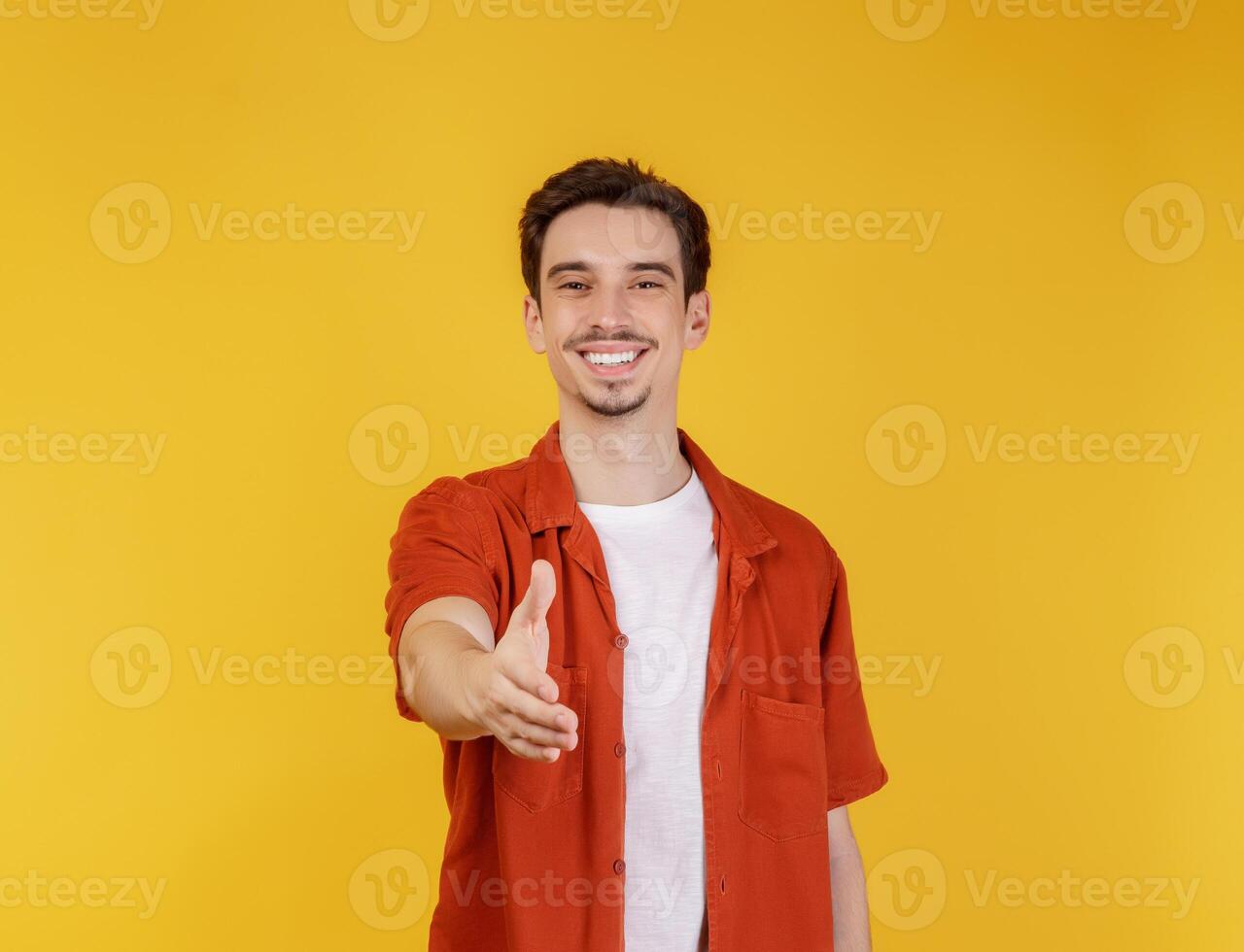 Portrait of smiling handsome man extend hand for handshake, look friendly, greet you, hi gesture, standing over yellow background photo