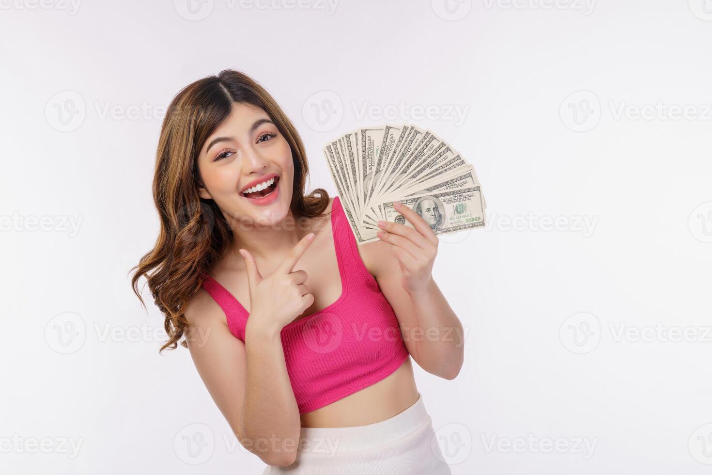 Portrait of excited young woman holding bunch of dollars banknotes and pointing finger at money isolated over white background photo