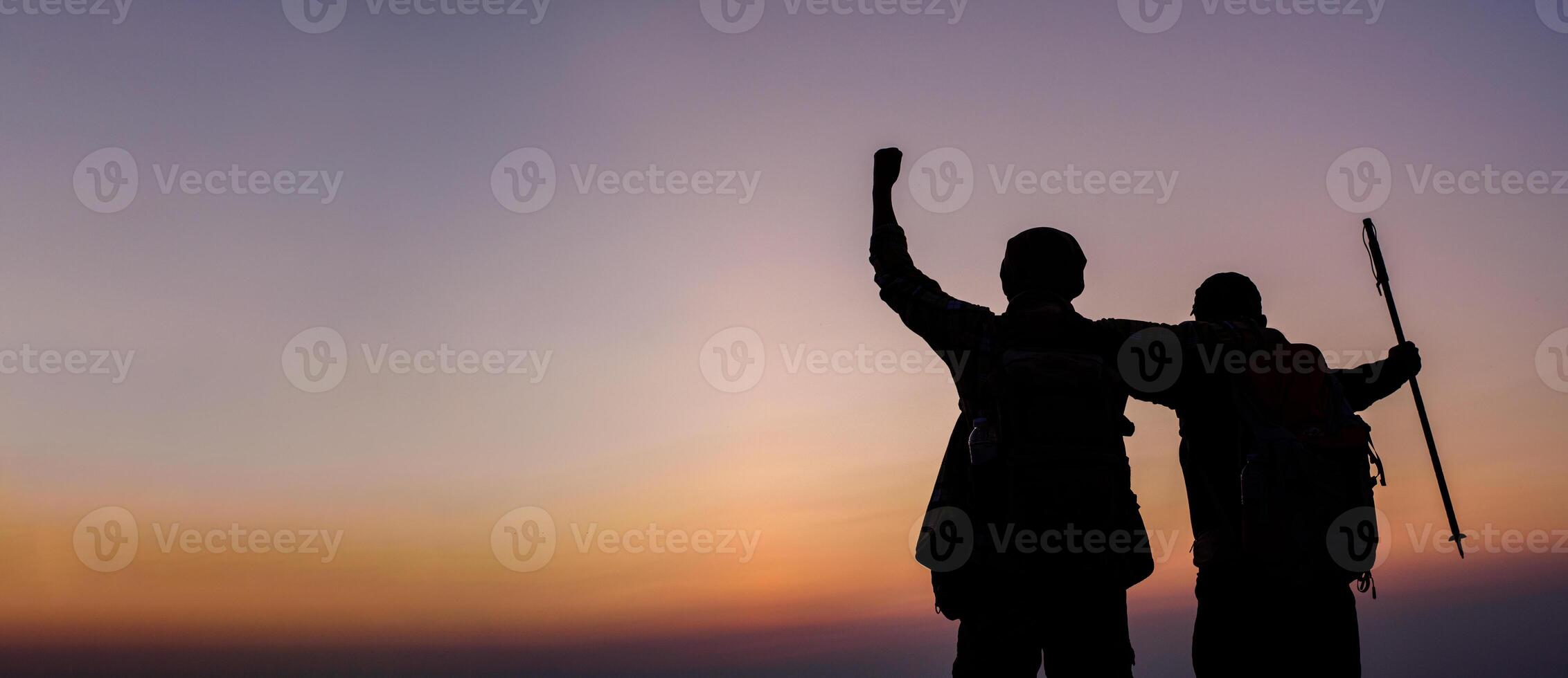Silhouette of cheering hiking couple open arms to the sunrise stand at on mountain photo