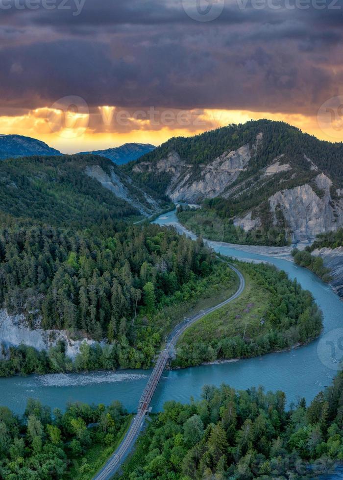 A river that runs in a S curve between the mountains,a railroad bridge crosses the river photo