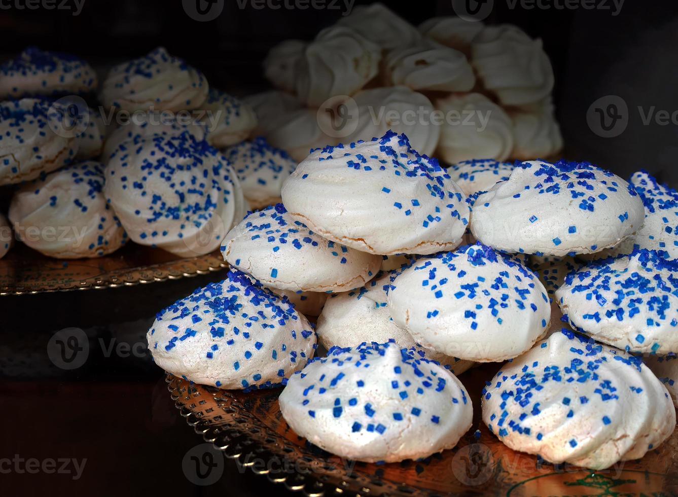 Close up crumbly Meringues cookies sprinkle with blue sugar chips on top on beautiful tray in pastry shop, Portugal dessert sweets, confectionery concept photo