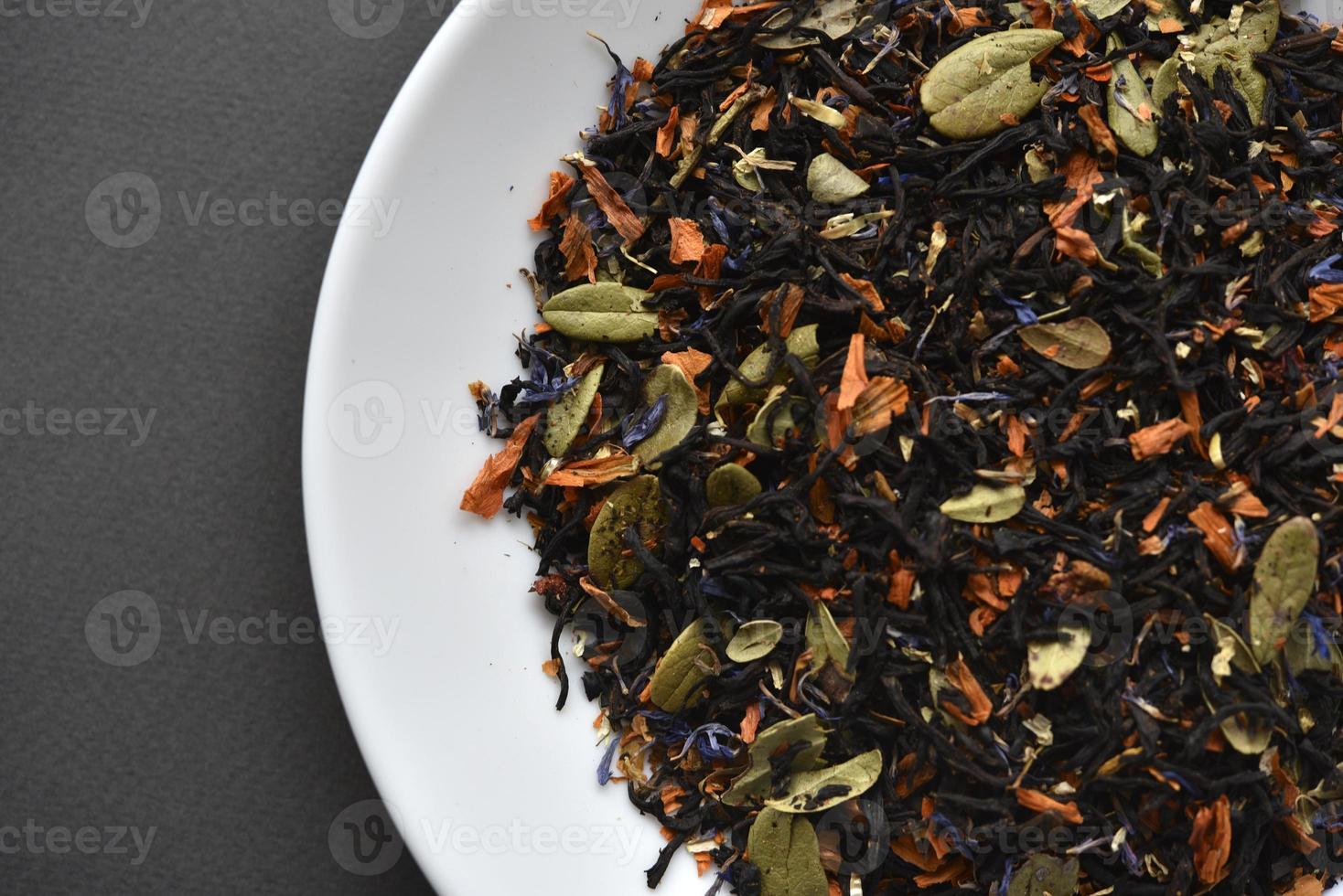 Black tea on a white plate. Dry tea with spices for brewing. photo