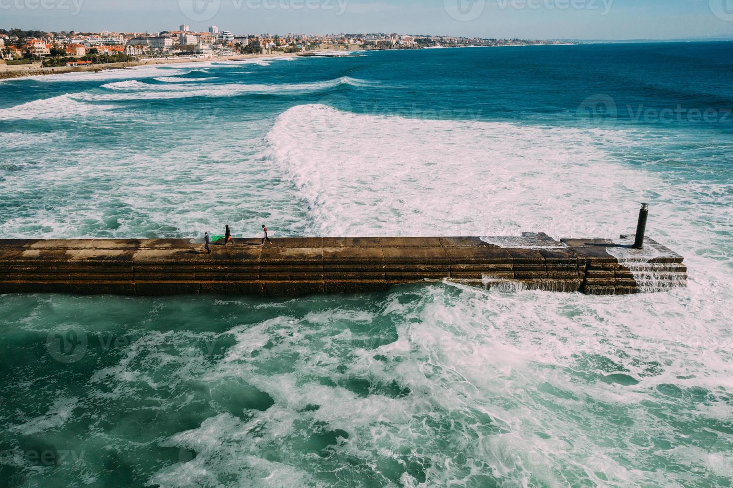 Surfers carrying their boards at a pier in Cascais, Portugal with giant swell visible photo