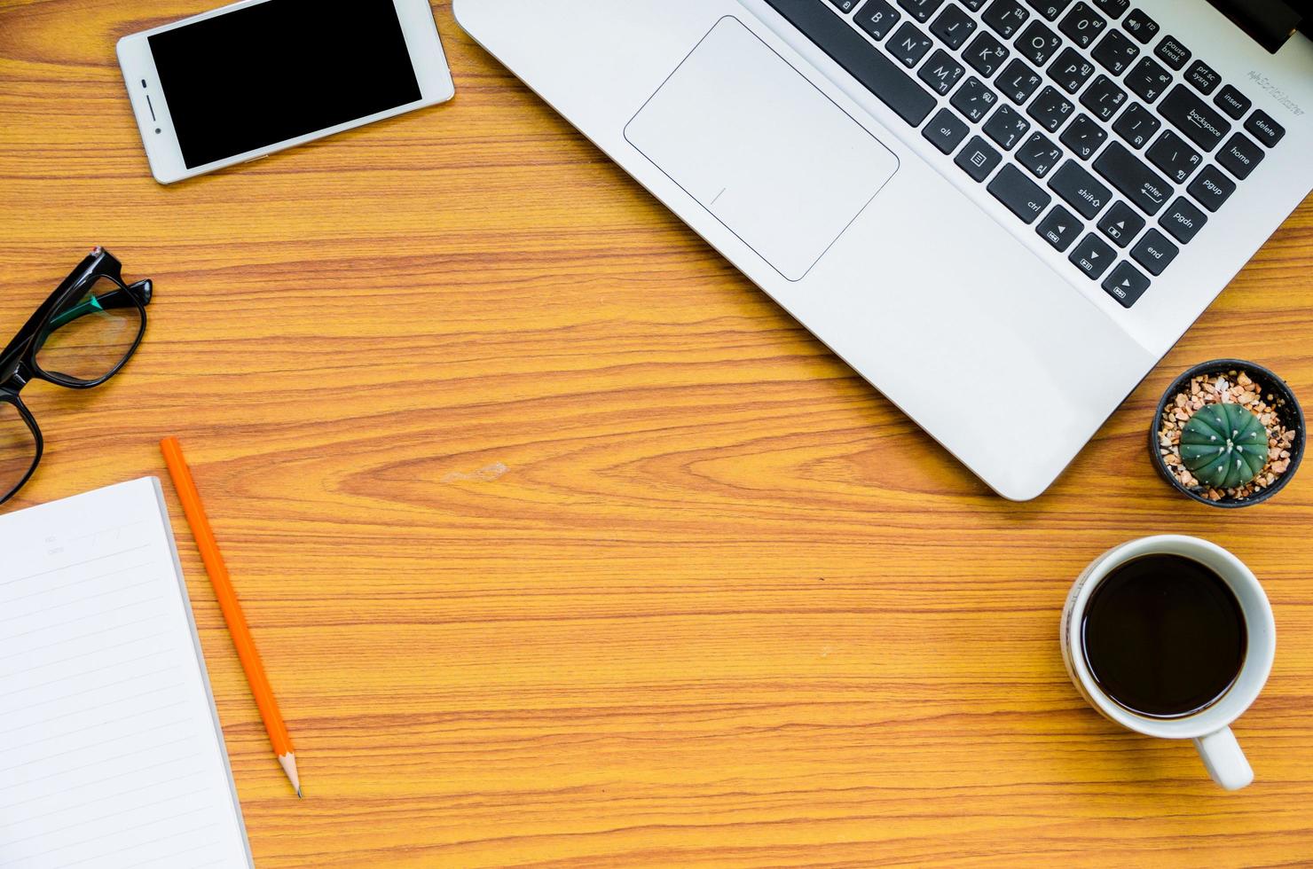 laptop on wooden table with coffee cup, phone, book, glasses and cactus on top view with space in center photo