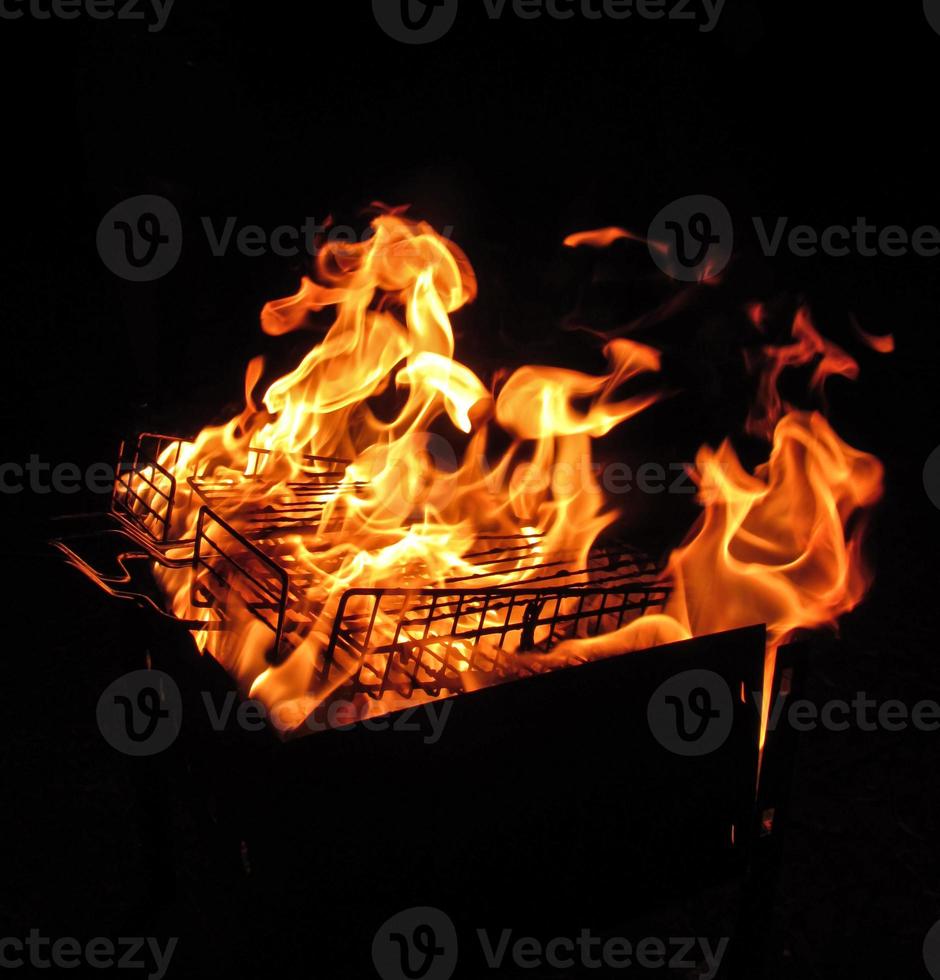 Metal net over fire burning coal ember wood in barbecue grill at night photo