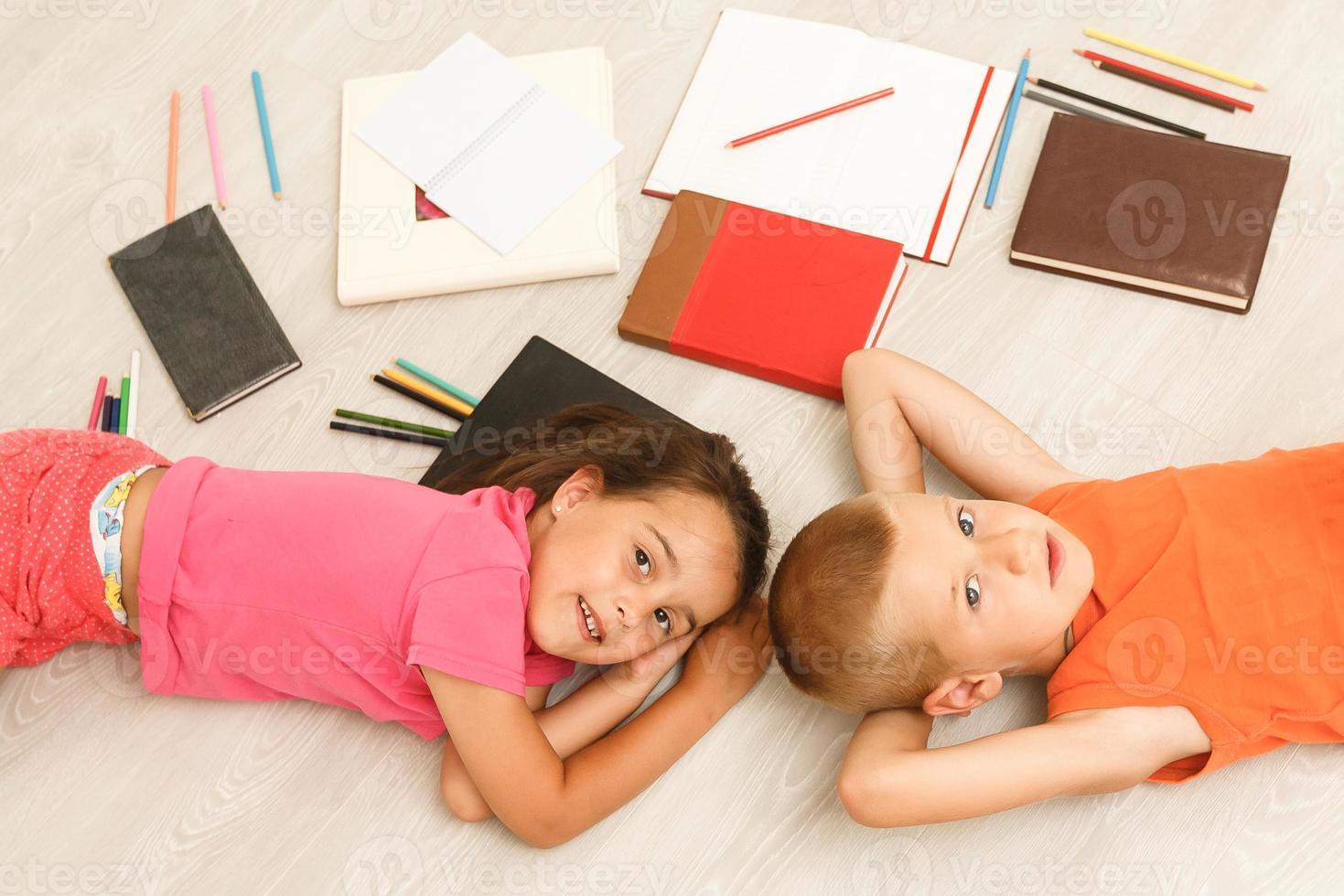 Happy children. Top view creative photo of little boy and girl on vintage brown wooden floor. Children lying near books and toys, and painting