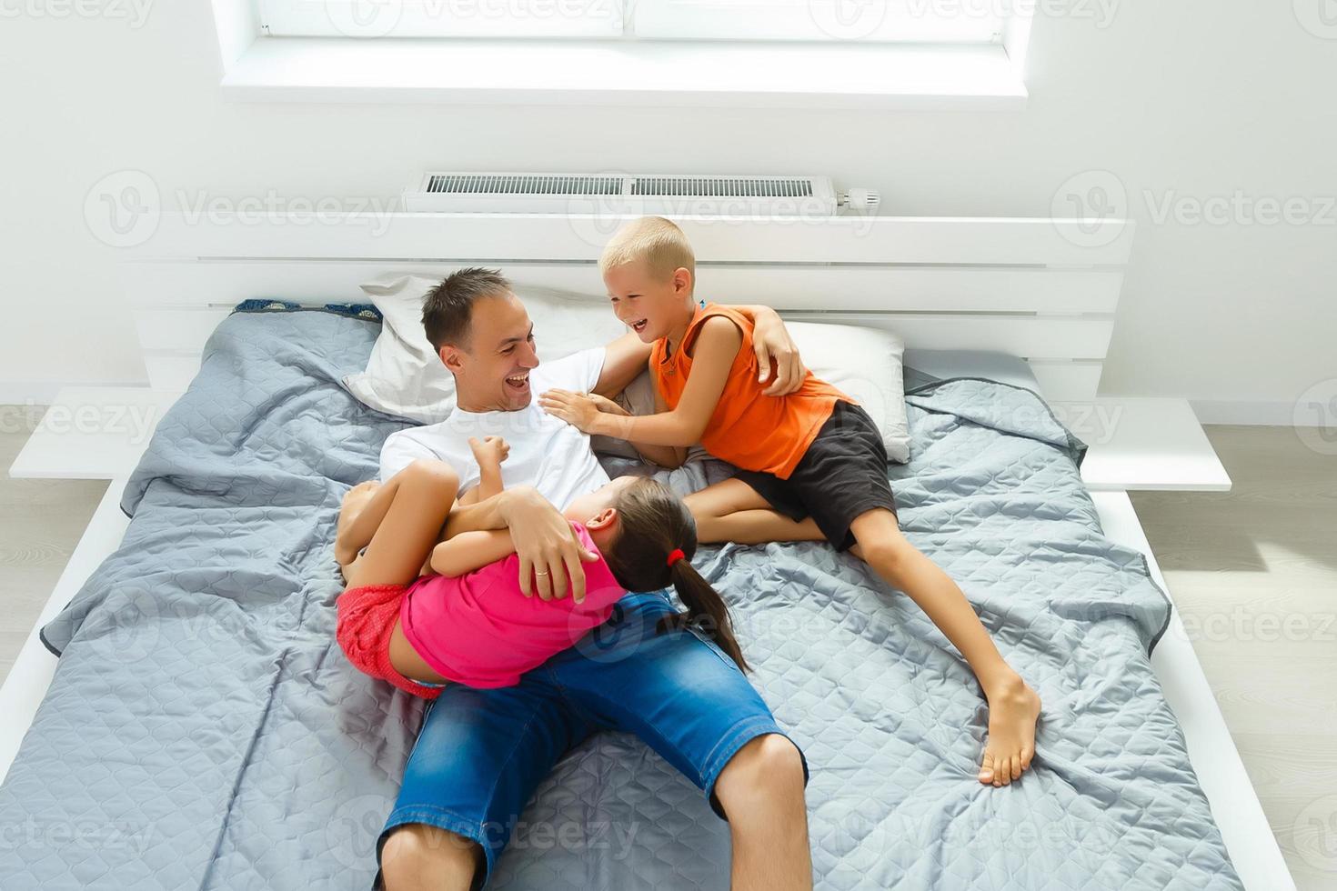 joven padre jugando con bebé hija como acostado en sofá a hogar, sonriente contento teniendo divertida. lado vista. foto