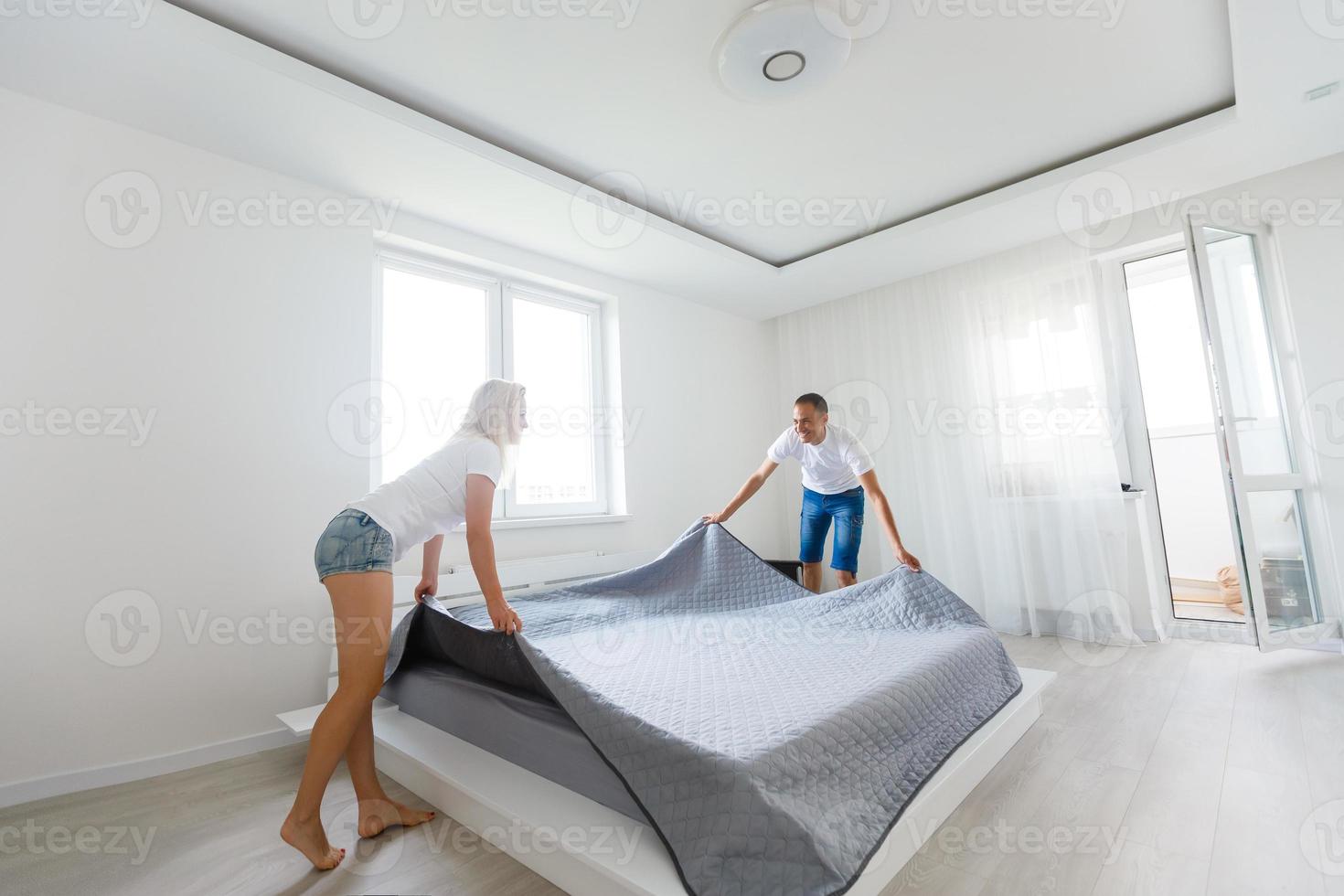 Portrait of young attractive cute couple together on bed in the morning, wearing pajama, covered, wrapped in blanket, girl smiling, guy kissing the lady in apartment, leisure photo