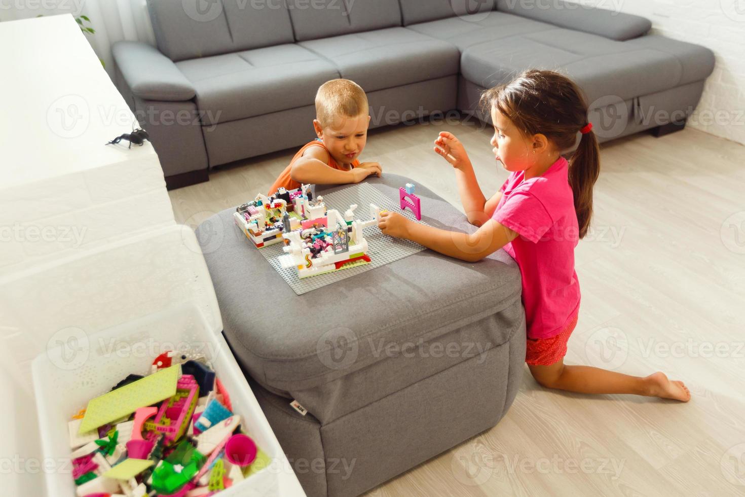 Three active barefooted Caucasian kids wearing similar clothes celebrating funny birthday party in living room, dancing, standing in conga line one after another, playing indoor games, feeling happy photo