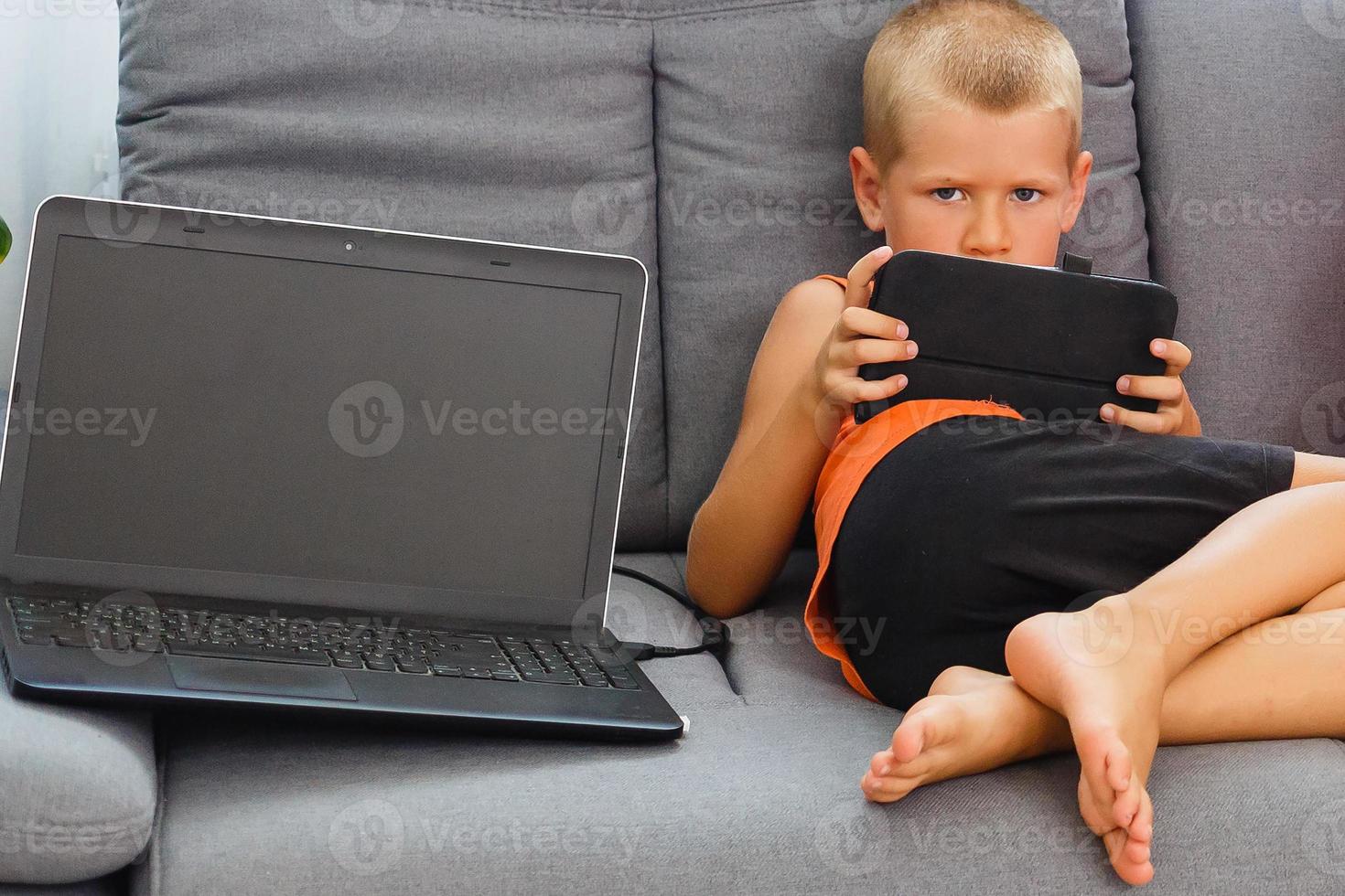 Little boy with digital tablet sitting on sofa, on home interior background photo